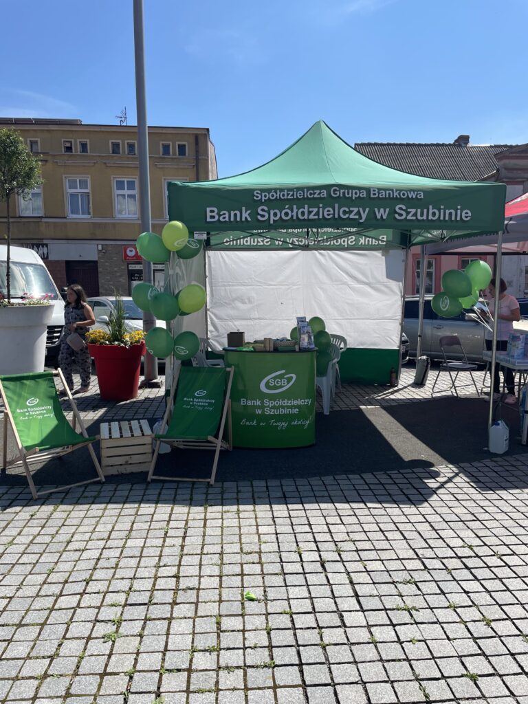 Stoisko Banku Spółdzielczego w Szubinie z zielonym namiotem i balonami, promujące lokalne usługi bankowe.