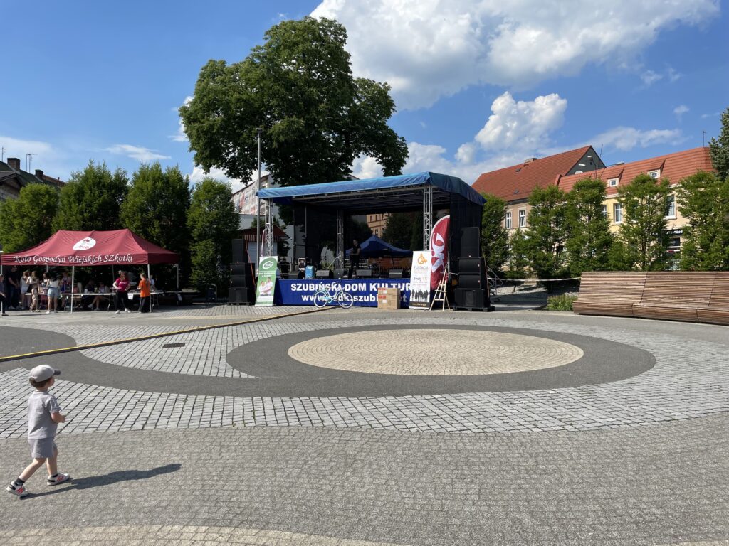 Scena z wydarzenia kulturalnego w Szubinie, ludzie w tle, dzieci bawią się na świeżym powietrzu.