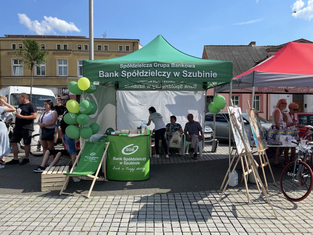 Stoisko Banku Spółdzielczego w Szubinie z zielonymi balonami i uczestnikami na wydarzeniu plenerowym.