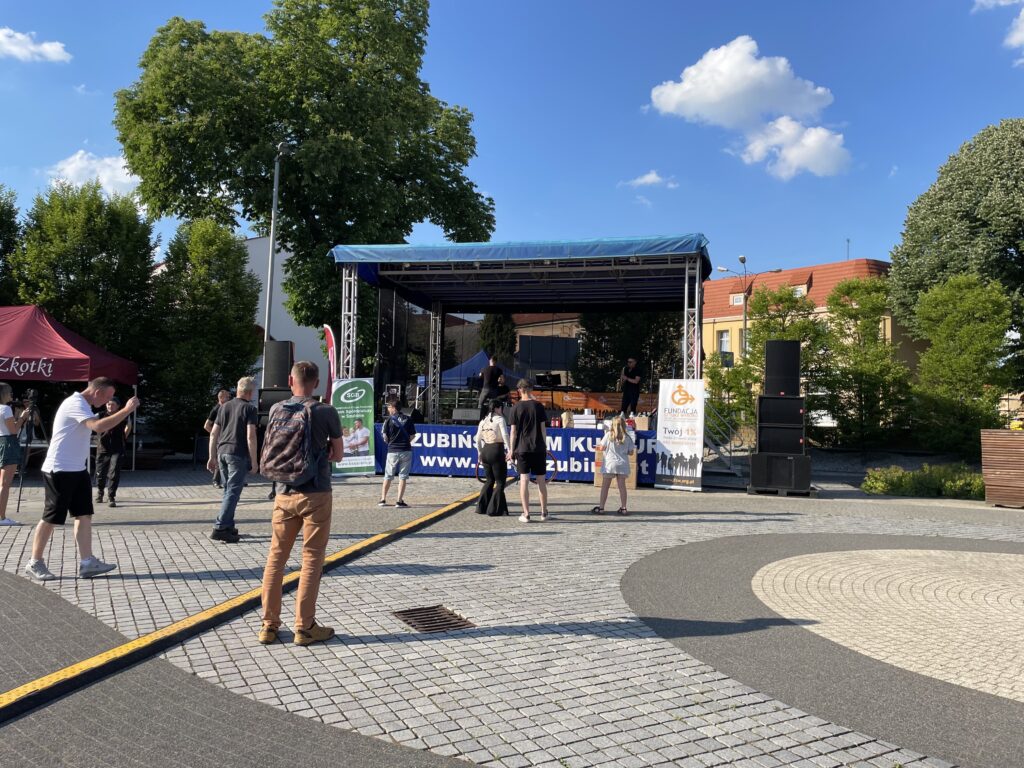 Ludzie uczestniczą w wydarzeniu kulturalnym na zorganizowanej scenie plenerowej w Złotoryi.