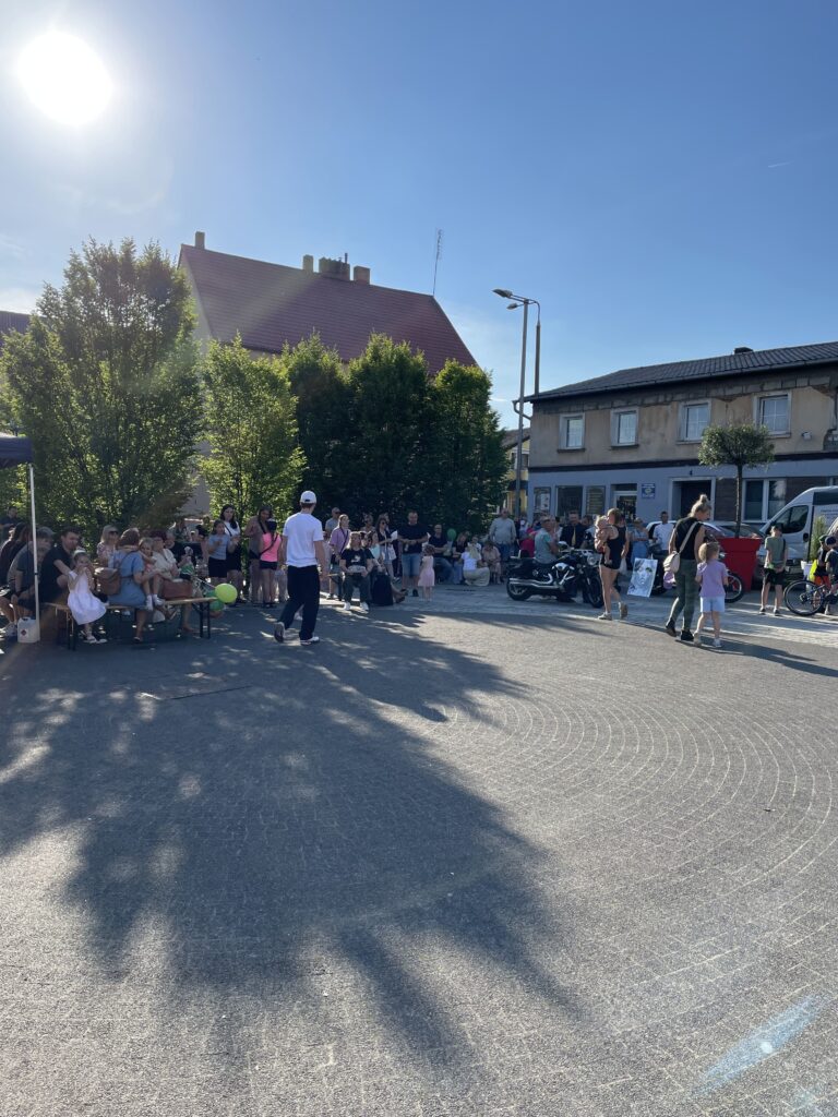 Tłum ludzi na ulicy w słoneczny dzień, uczestniczący w lokalnym wydarzeniu lub festiwalu.