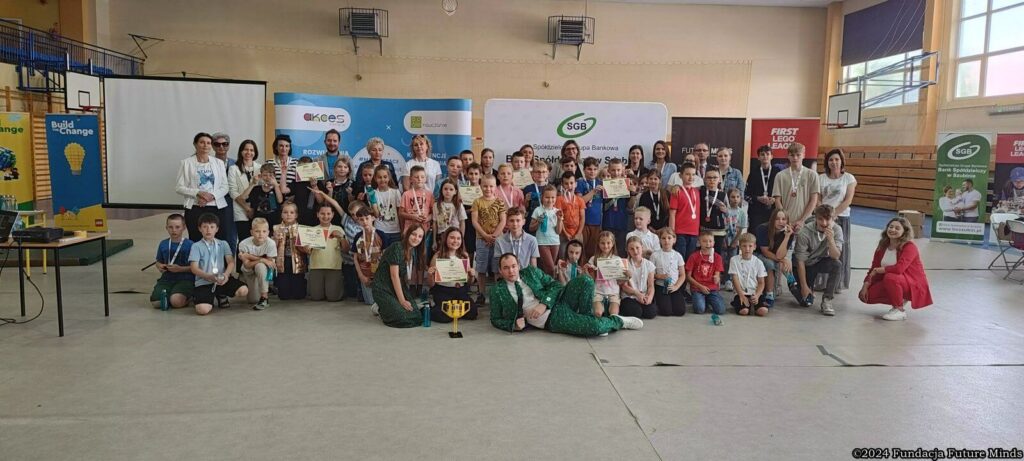 Uczestnicy konkursu edukacyjnego z nagrodami, pamiątkami i dyplomami w sali sportowej.