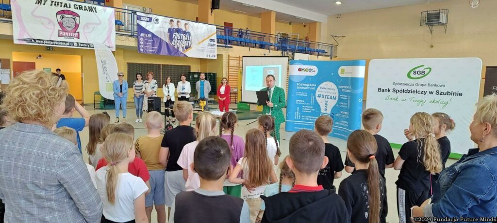 Uczestnicy wydarzenia w hali sportowej, z prelegentami i organizatorami, promujący edukację i sport.