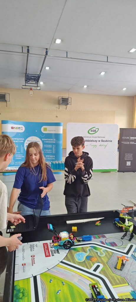 Młodzież pracuje z robotami w trakcie warsztatów edukacyjnych w szkole. Uczestnicy korzystają z laptopów.